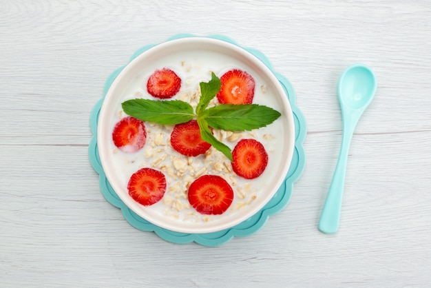 Latte di vista superiore con la farina d'avena dentro il piatto con le fragole su bianco, salute dei cereali da prima colazione deliziosa