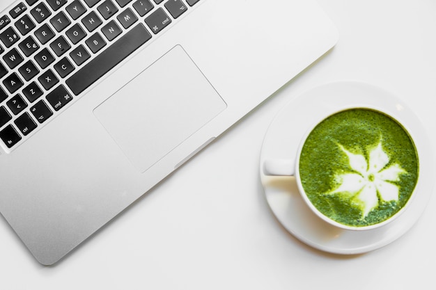 Latte giapponese del tè verde in tazza bianca vicino al computer portatile sullo scrittorio bianco