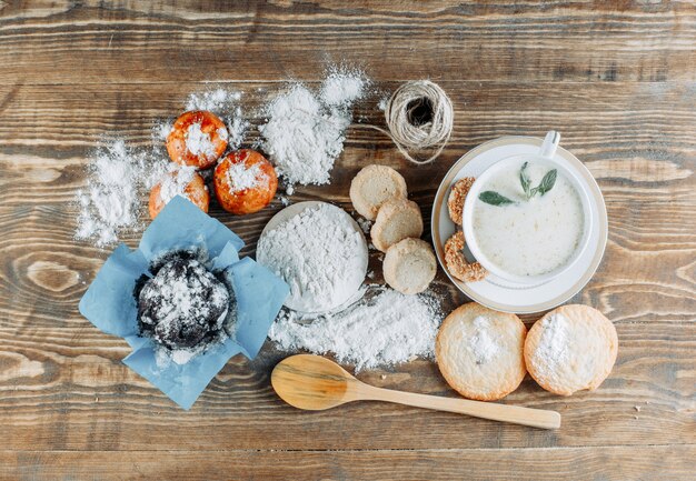 Latte piccante in una tazza con biscotti, cucchiaio, corda, vista dall'alto di zucchero a velo su una superficie di legno