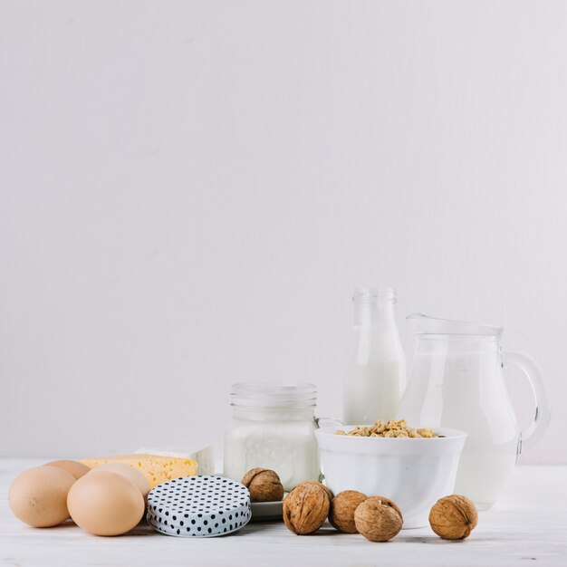 Latte; uova; ciotola di cereali; formaggio e noci su sfondo bianco