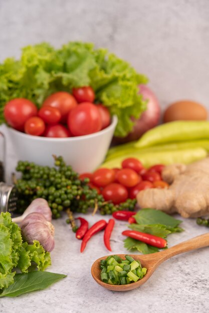 Lattuga e pomodori in una tazza bianca con cipolle affettate e peperoni freschi sul pavimento di cemento.