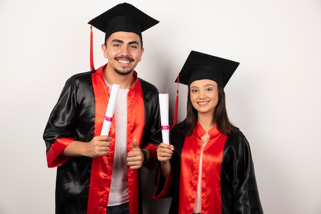 Laureati freschi con diploma in piedi su bianco.