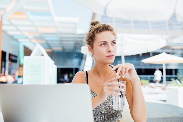 Lavorare all'aperto. Bella donna in cappello funky che lavora al computer portatile e che sorride mentre sedendosi all'aperto