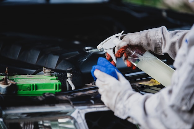 Lavoratore dell'autolavaggio che indossa un'uniforme bianca che sta una spugna per pulire l'automobile nel centro dell'autolavaggio, concetto per industria di cura di automobile.