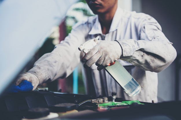 Lavoratore dell'autolavaggio che indossa un'uniforme bianca che sta una spugna per pulire l'automobile nel centro dell'autolavaggio, concetto per industria di cura di automobile.