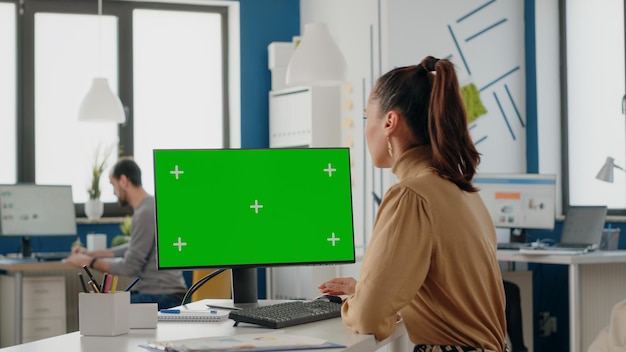 Lavoratore dell'azienda che utilizza un computer con schermo verde in ufficio. Donna d'affari che lavora con mock up modello isolato e sfondo bianco chiave cromatica. App Greenscreen sul monitor con spazio di copia