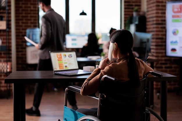 Lavoratore dell'azienda con disabilità fisica che parla al telefono fisso, conversa a distanza sul telefono dell'ufficio. Utente su sedia a rotelle con condizioni di salute croniche in chat al telefono.