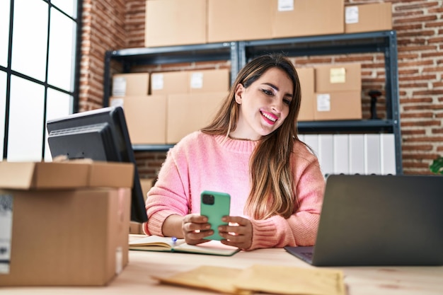 Lavoratore di affari di commercio elettronico della giovane bella donna ispanica che utilizza smartphone all'ufficio