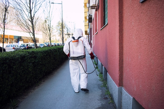 Lavoratore in tuta di protezione chimica che spruzza disinfettante su superfici pubbliche