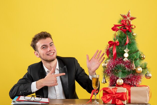 Lavoratore maschio vista frontale seduto dietro il suo posto di lavoro su giallo