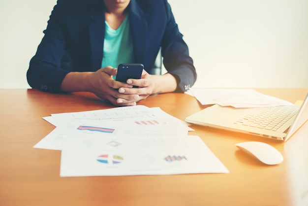 Lavoratore scrittura in un telefono con il computer portatile e documenti