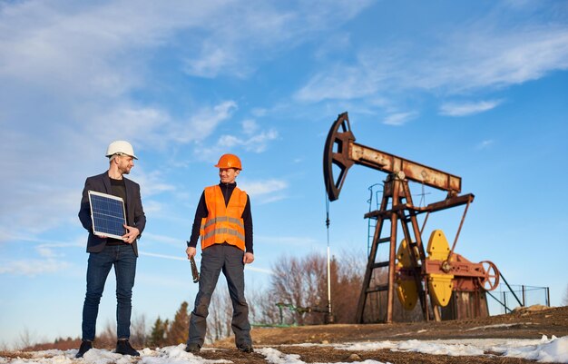 Lavoratori petroliferi in piedi sul territorio del giacimento di petrolio con martinetto della pompa