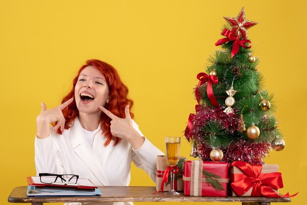 lavoratrice seduta dietro il suo tavolo con albero di Natale e regali su giallo