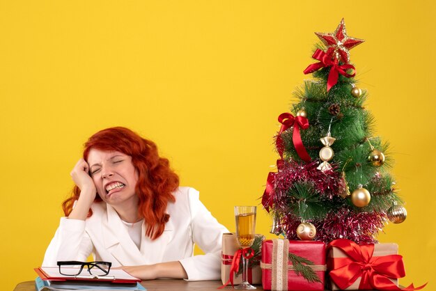lavoratrice seduta dietro il tavolo con regali di Natale e albero giallo