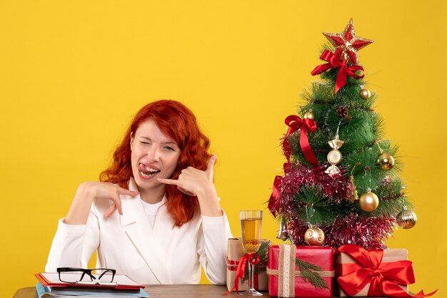 lavoratrice seduta dietro il tavolo con regali di Natale e albero giallo