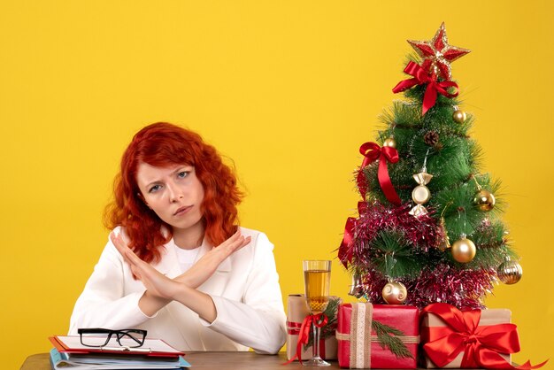 lavoratrice seduta dietro il tavolo con regali di Natale e albero giallo