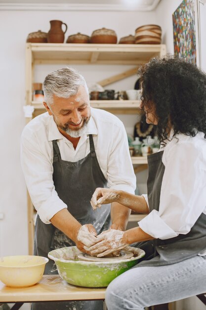 Lavoro creativo reciproco. Coppia elegante adulta in abiti casual e grembiuli. Persone che creano una ciotola su un tornio in uno studio di argilla.