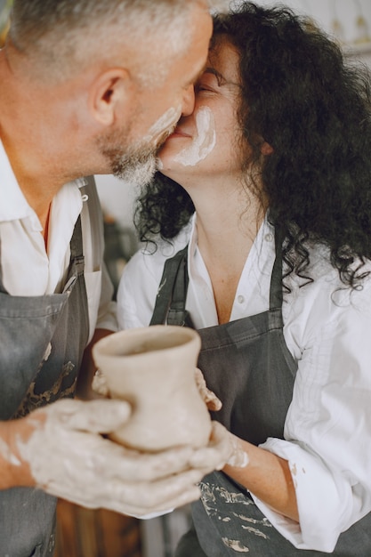 Lavoro creativo reciproco. Coppia elegante adulta in abiti casual e grembiuli. Persone che creano una ciotola su un tornio in uno studio di argilla.