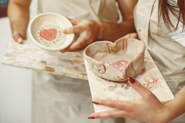 Lavoro creativo reciproco. Giovane bella coppia in abiti casual e grembiuli. La gente detiene piatti in ceramica.