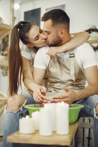 Lavoro creativo reciproco. Giovane bella coppia in abiti casual e grembiuli. Persone che creano una ciotola su un tornio in uno studio di argilla.