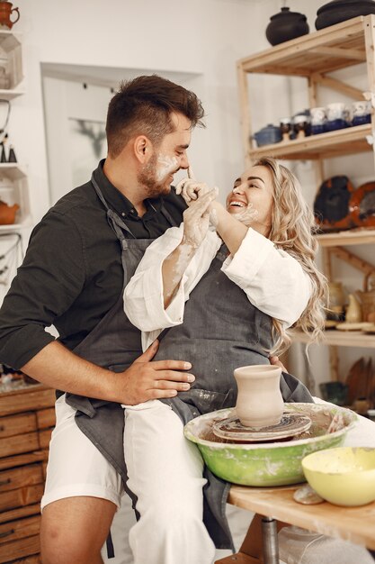 Lavoro creativo reciproco. Giovane bella coppia in abiti casual e grembiuli. Persone che creano una ciotola su un tornio in uno studio di argilla.