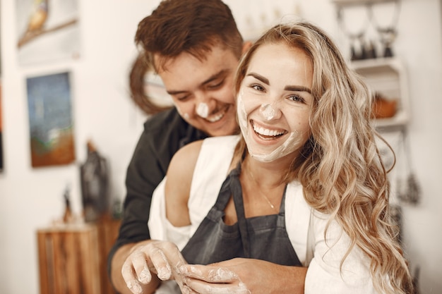 Lavoro creativo reciproco. Giovane bella coppia in abiti casual e grembiuli. Persone che creano una ciotola su un tornio in uno studio di argilla.