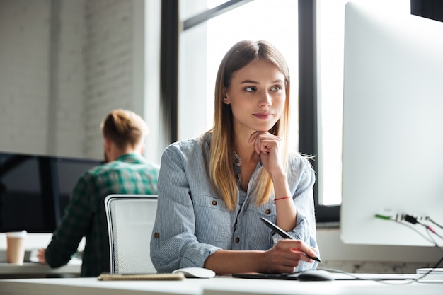 Lavoro della giovane donna in ufficio facendo uso del computer e della tavola del grafico