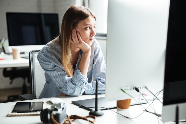 Lavoro serio della giovane donna in ufficio facendo uso del computer