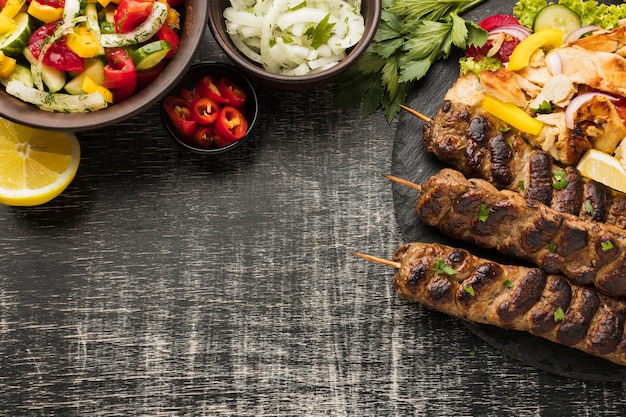 Lay piatto di gustosi kebab su ardesia con altri piatti e verdure