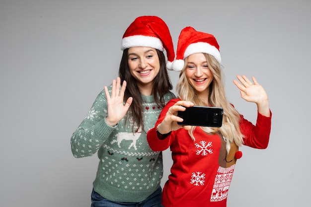 Le amiche attraenti in cappelli di natale rossi e bianchi posano per selfie