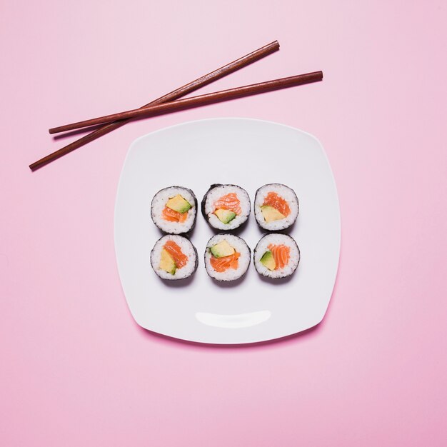 Le bacchette si avvicinano ai sushi sul rosa