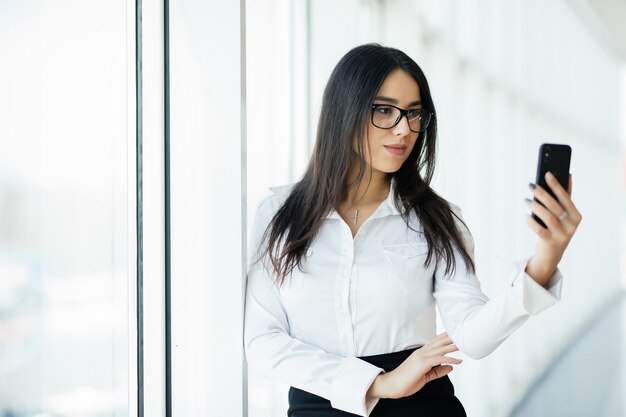 Le belle donne usano il telefono alla finestra panoramica. Concetto di affari