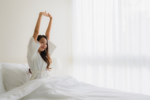 Le belle giovani donne asiatiche del ritratto sorridono felici sul letto