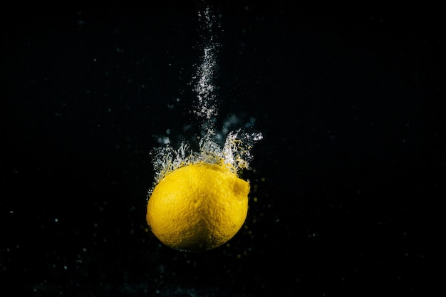 Le bolle si alzano intorno al limone giallo che cade nell&#39;acqua