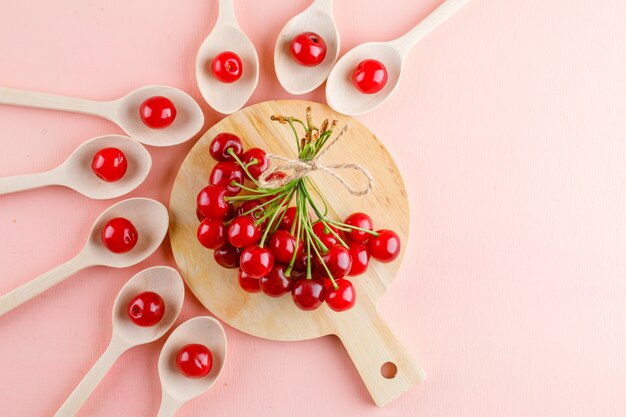Le ciliegie in cucchiai di legno piatti giacciono sul rosa e sul tagliere