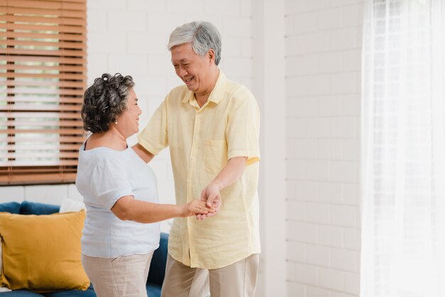 Le coppie anziane asiatiche che ballano insieme mentre ascoltano la musica in salone a casa, coppie dolci godono del momento di amore mentre si divertono una volta rilassato a casa.