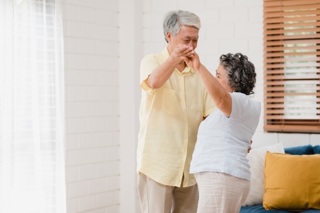 Le coppie anziane asiatiche che ballano insieme mentre ascoltano la musica in salone a casa, coppie dolci godono del momento di amore mentre si divertono una volta rilassato a casa.