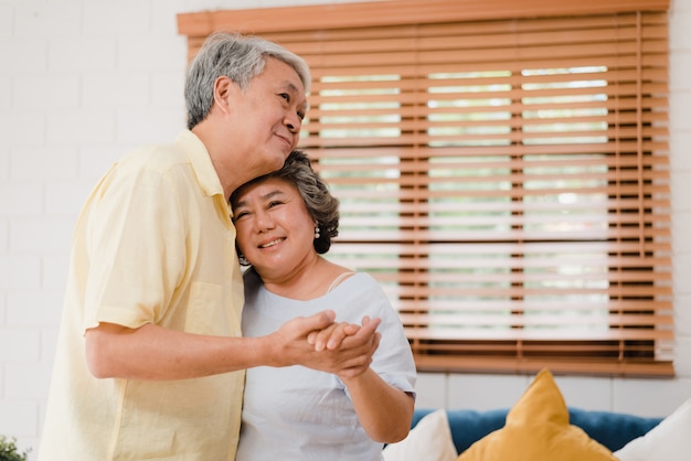 Le coppie anziane asiatiche che ballano insieme mentre ascoltano la musica in salone a casa, coppie dolci godono del momento di amore mentre si divertono una volta rilassato a casa.