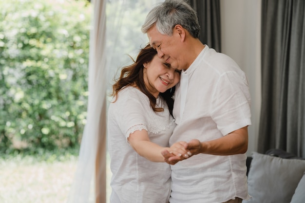 Le coppie anziane asiatiche che ballano insieme mentre ascoltano la musica nel salone a casa, le coppie dolci godono del momento di amore divertendosi quando si rilassano a casa. La famiglia senior di stile di vita si rilassa a casa il concetto.