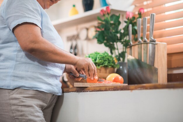 Le coppie anziane asiatiche tagliano i pomodori preparano l&#39;ingrediente per la fabbricazione dell&#39;alimento nella cucina