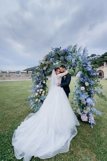 Le coppie attraenti di nozze nell'amore sta stando all'aperto vicino al bello arco fatto dei fiori blu