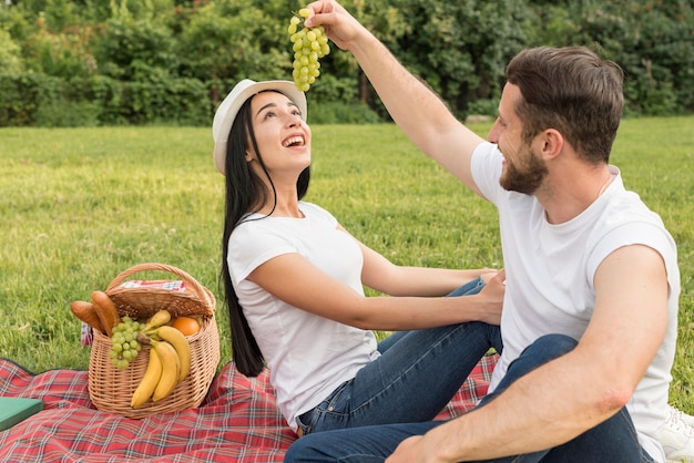 Le coppie che mangiano l&#39;uva con una coperta di picnic