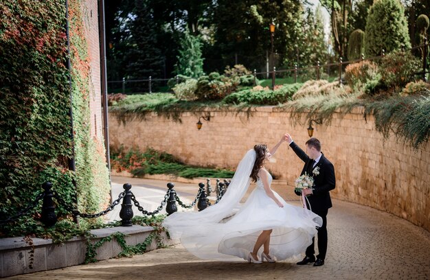 Le coppie di nozze stanno ballando vicino al muro di pietra coperto di edera verde