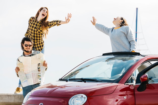 Le donne allegre che danno cinque si avvicinano all&#39;uomo che esamina la mappa vicino all&#39;automobile