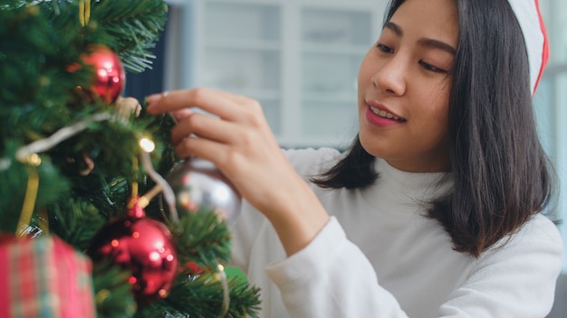 Le donne asiatiche decorano l'albero di Natale al festival di Natale. Il sorridere felice teenager femminile celebra le vacanze invernali di natale in salone a casa. Colpo da vicino.