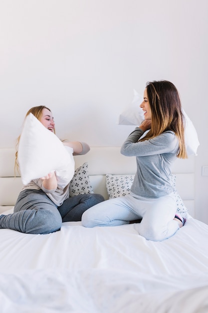 Le donne attraenti che hanno cuscino combattono sul letto