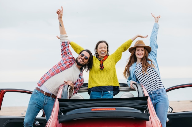 Le donne sorridenti si avvicinano all&#39;uomo felice con le mani alzate che si sporgono dall&#39;automobile