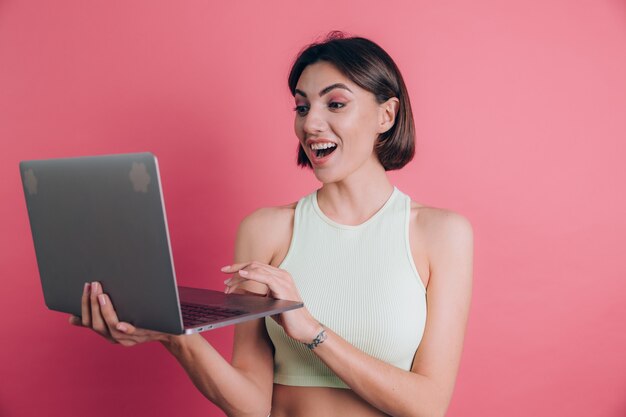 Le donne su sfondo rosa mantenendo la bocca aperta tenere il computer portatile