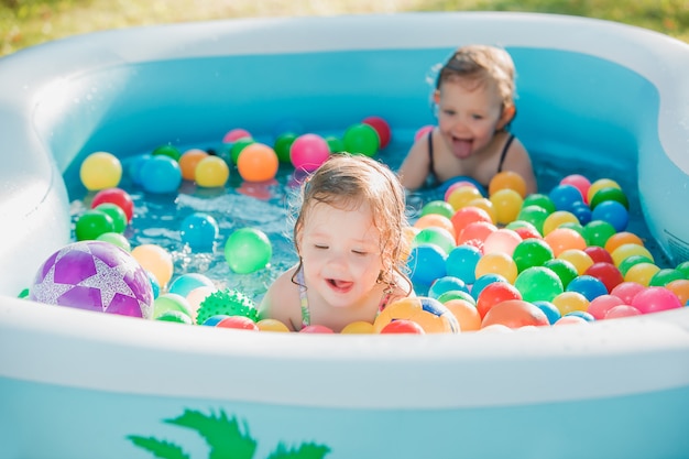 Le due bambine che giocano con i giocattoli in piscina gonfiabile in giornata di sole estivo