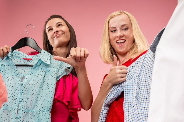 Le due giovani belle ragazze che guardano i vestiti e provano mentre scelgono in negozio